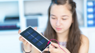 A young girl connecting cables to a small photovoltaic panel