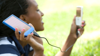 jeune femme rechargeant son portable grâce à sa batterie solaire