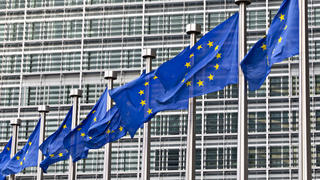 Image of the European Union headquarters in Brussels, behind a row of European flags.
