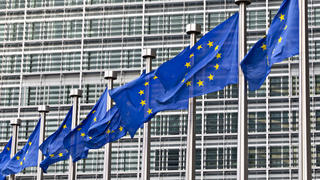 Image du siège de l’Union européenne à Bruxelles, derrière une rangée de drapeaux de l’Europe.