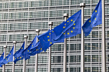 Image of the European Union headquarters in Brussels, behind a row of European flags.